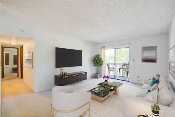 A living room with a white couch, a white chair, a wooden coffee table, a flat screen TV, and a plant.