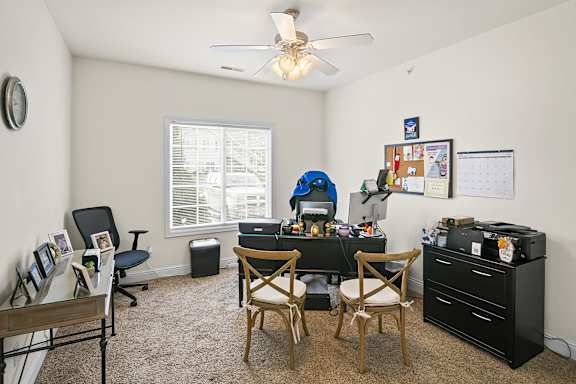 A room with a desk, chairs, and a ceiling fan.