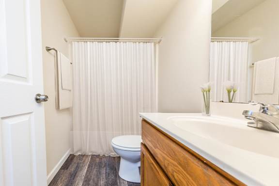 A white toilet sits in a bathroom with a white sink and a white shower curtain.