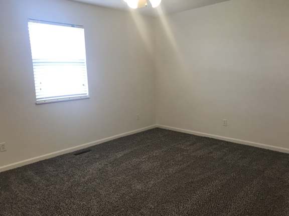 A room with a carpeted floor and a window letting in sunlight.