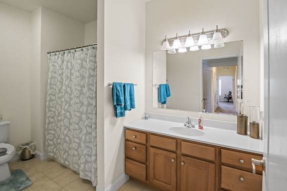 A bathroom with a white sink, brown drawers, and a shower with a blue shower curtain.