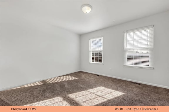 A room with a carpeted floor and two windows.