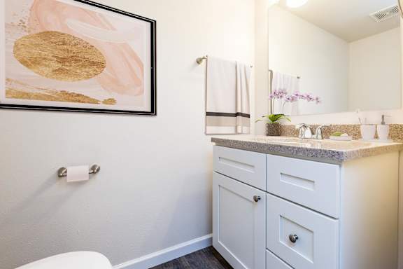 A bathroom with a white toilet and a white cabinet with a gold and white painting above it.