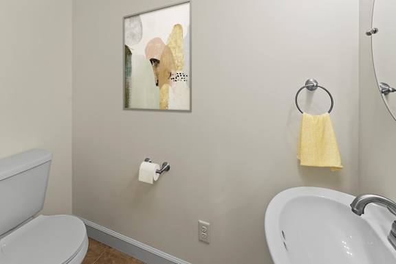 A bathroom with a toilet, sink, and a painting hanging on the wall.