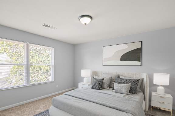 A bedroom with a large bed, two lamps, and a painting on the wall.