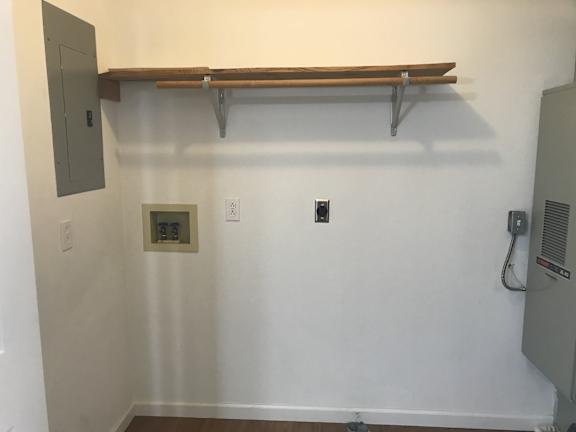A white wall with a brown shelf and a grey electrical box.