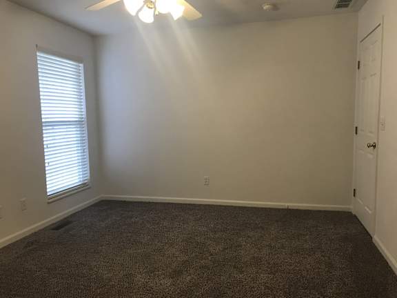 A room with a carpeted floor, a ceiling fan, and a window with blinds.