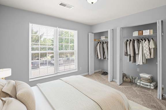 A bedroom with a large bed and a closet with clothes hanging.