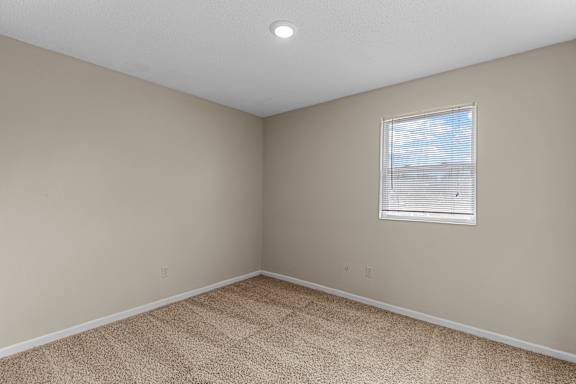 A room with a carpeted floor and a window with blinds.