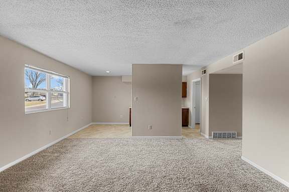 A spacious room with beige carpeting and a window overlooking a street.