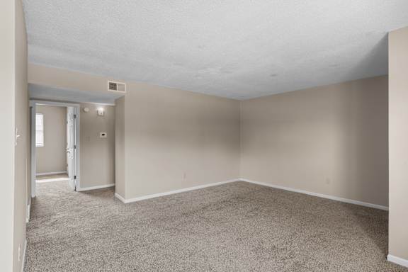 A large, empty room with carpeted flooring and a doorway leading to another room.