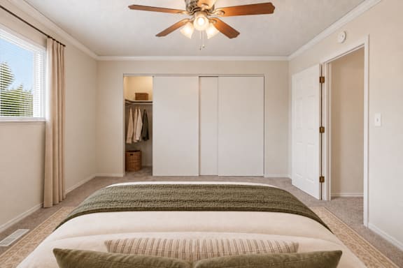 A bedroom with a bed, a ceiling fan, and a closet.