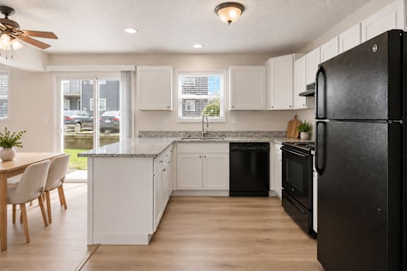 A black refrigerator is in the corner of a kitchen with white cabinets.