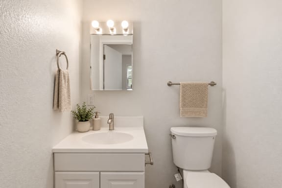 A white bathroom with a toilet, sink, mirror, and towel rack.
