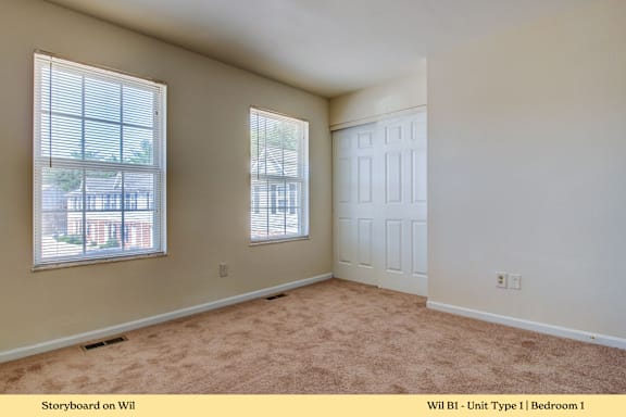 A bedroom with a carpeted floor and a window.
