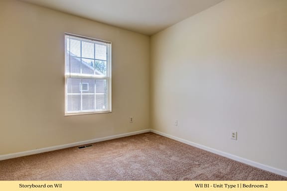A bedroom with a window and carpeted floor.