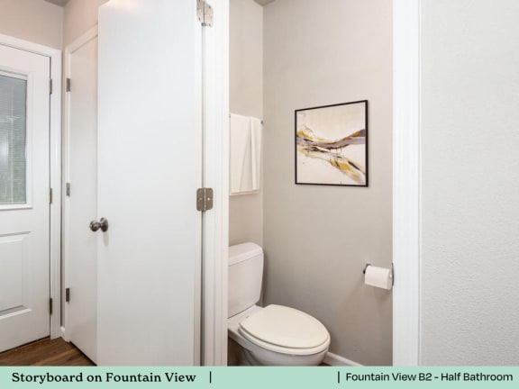 A white toilet in a small bathroom with a picture on the wall.