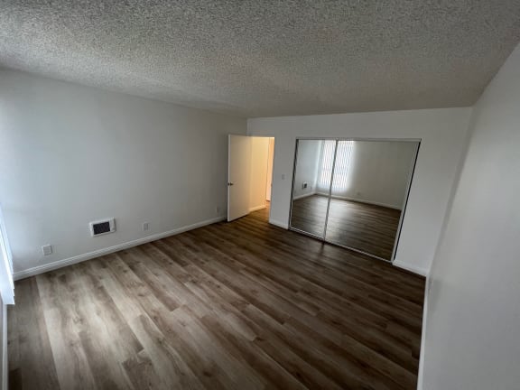 an empty living room with wood flooring and a mirrored closet