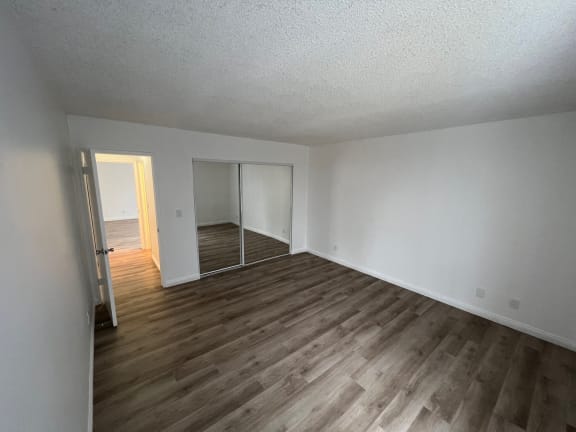 an empty living room with wood flooring and a mirrored closet