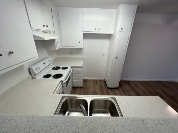 an empty kitchen with white cabinets and a stainless steel sink