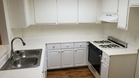 A white kitchen with a stove, sink, and cabinets.