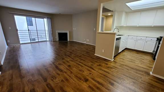 A spacious living room with hardwood floors and a kitchen area with white cabinets.