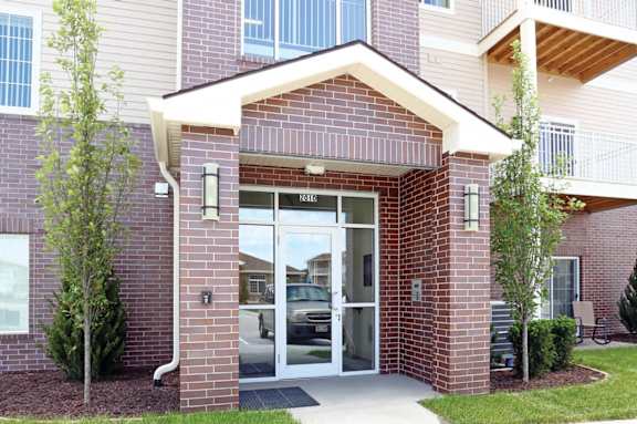 The front entrance of a brick building with a glass door and a small porch.