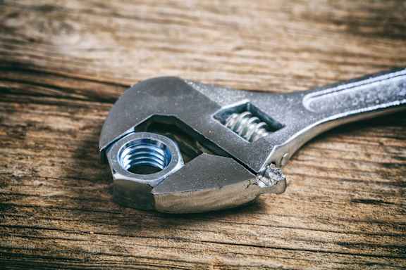 A silver wrench with a nut on a wooden surface.