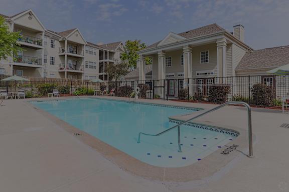 A swimming pool in front of a building with a black fence around it.