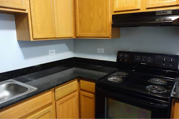 A black stove top oven with four burners is in a kitchen with wooden cabinets.