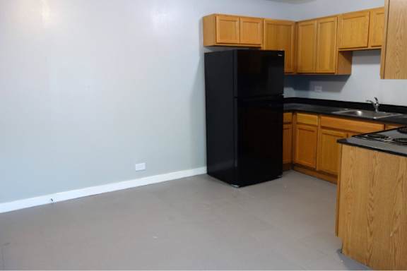 A black fridge sits in a kitchen with wooden cabinets.