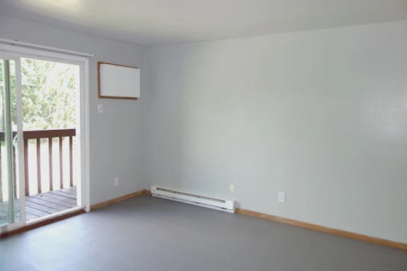 A room with a white wall and a window with a view of trees.