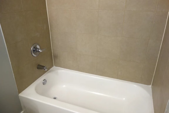 A white bathtub is in a bathroom with beige tiles.