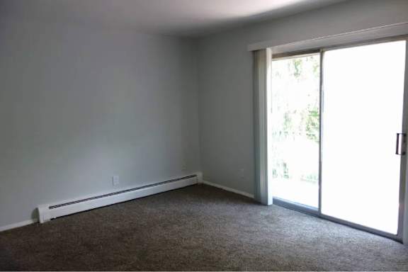 A room with a carpeted floor and a sliding glass door leading to a garden.