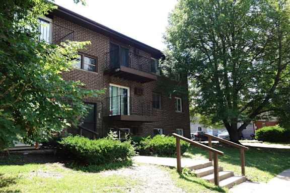 A brown brick building with a balcony and a tree in front.
