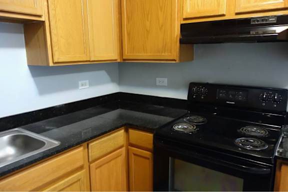 A black stove top oven with four burners is in a kitchen with wooden cabinets.
