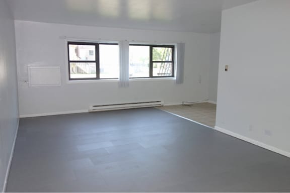A large empty room with a window and a radiator on the wall.