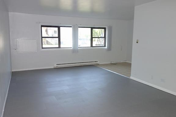 A large empty room with a window and a radiator on the wall.