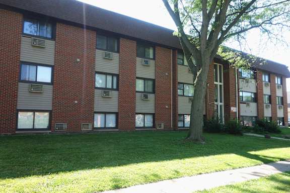 A tree is in front of a building with a lawn in front of it.