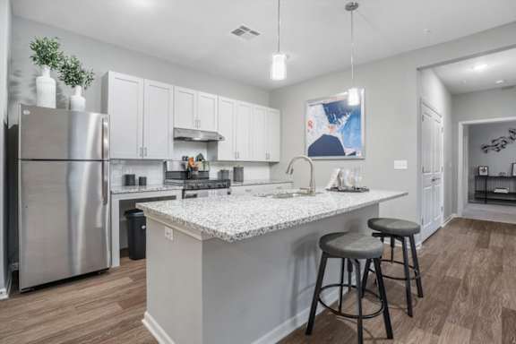A kitchen with a refrigerator, bar stools, and a countertop.