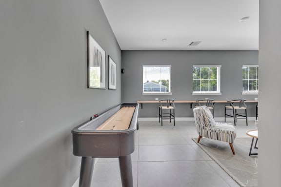 a room with a shuffle board table, a chair, and windows at Spire Luxury Apartments in Charlotte, NC