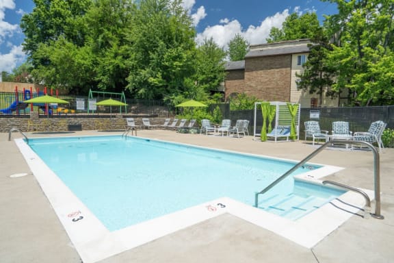 a swimming pool with chaise lounge chairs and umbrellas in front of a brick building at Stonewater Apartments, Louisville, KY