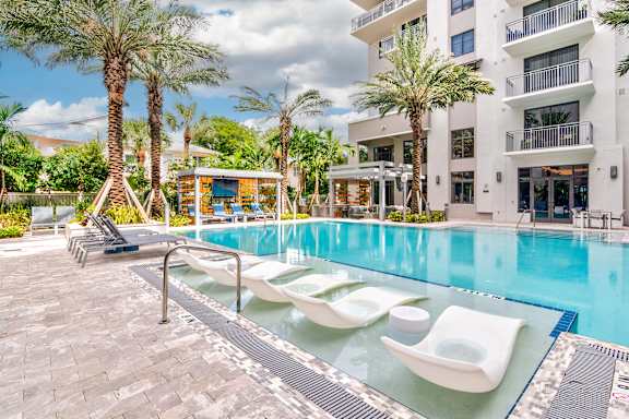 A pool with sun loungers and palm trees in front of a white building at Mayla Pompano, Pompano Beach, 33062