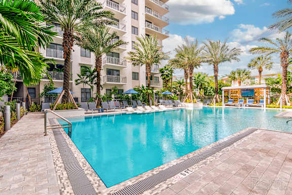 A large swimming pool surrounded by palm trees and a building in the background at Mayla Pompano, Pompano Beach, FL