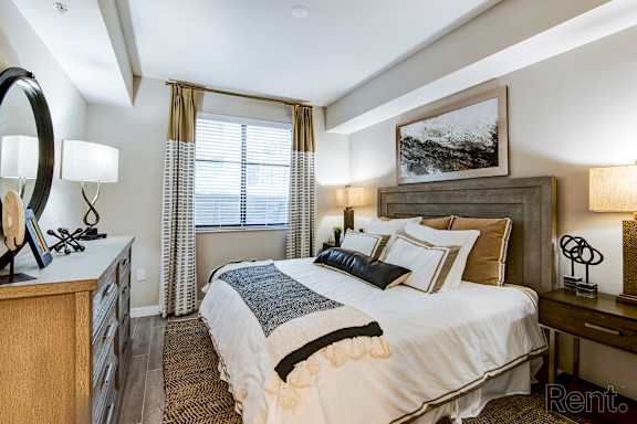 A well-lit bedroom with a large bed, a wooden dresser, and a framed picture on the wall.