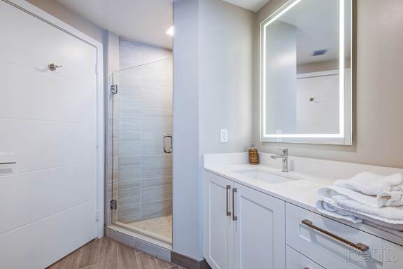 A white bathroom with a sink, mirror, and shower.