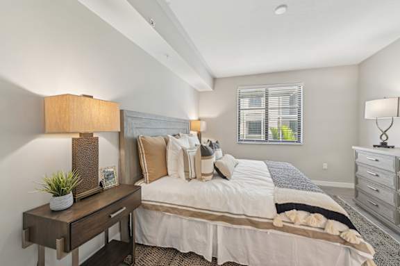 A well-lit bedroom with a large bed and a nightstand with a lamp.