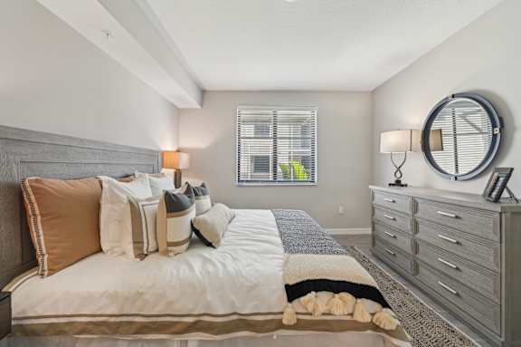 A bedroom with a bed, a dresser, and a window with blinds.