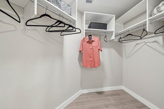 A pink shirt hanging on a hanger in a white closet.