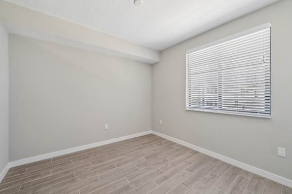 A room with a window covered by white blinds and wooden flooring.